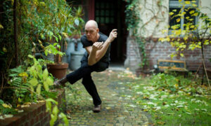 felix si regge su una gamba con braccia incorciata in una posa acrobatica, sfondo di un giardino selvatico