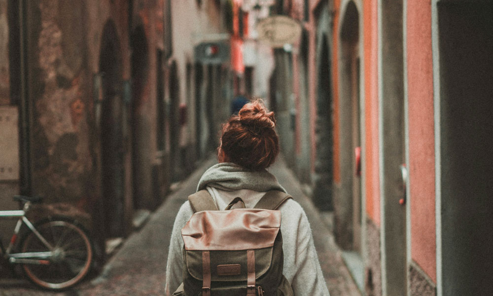 donna di spalle con azino e cappotto, capelli rossi a cipolla che cammina nelle strade di un paese