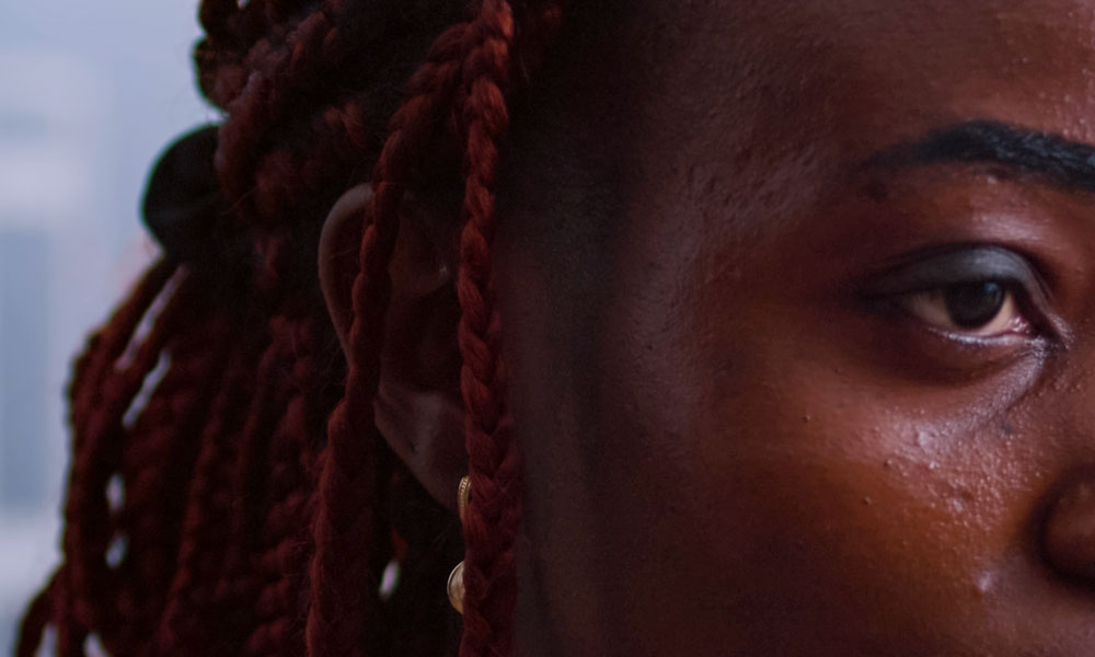 close-up di donna afrodiscendente, capelli con treccine rossastri e sguardo vacuo